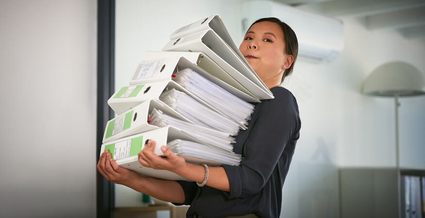 Woman carrying a large stack of binders full of printed paper