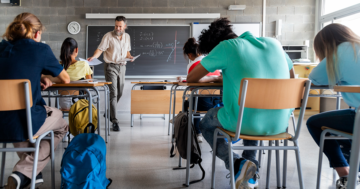 Teacher passing out printed pages to students 2